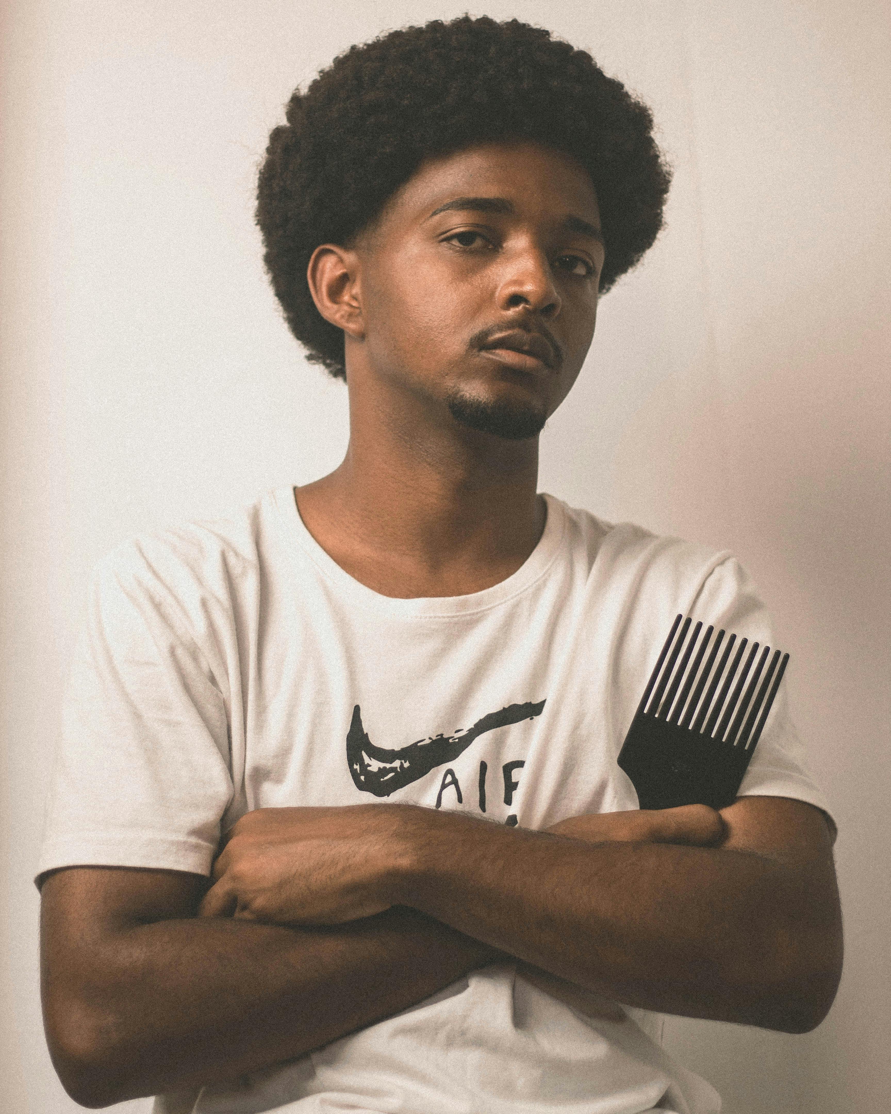 Young man with a natural afro standing with arms crossed, holding an afro pick comb