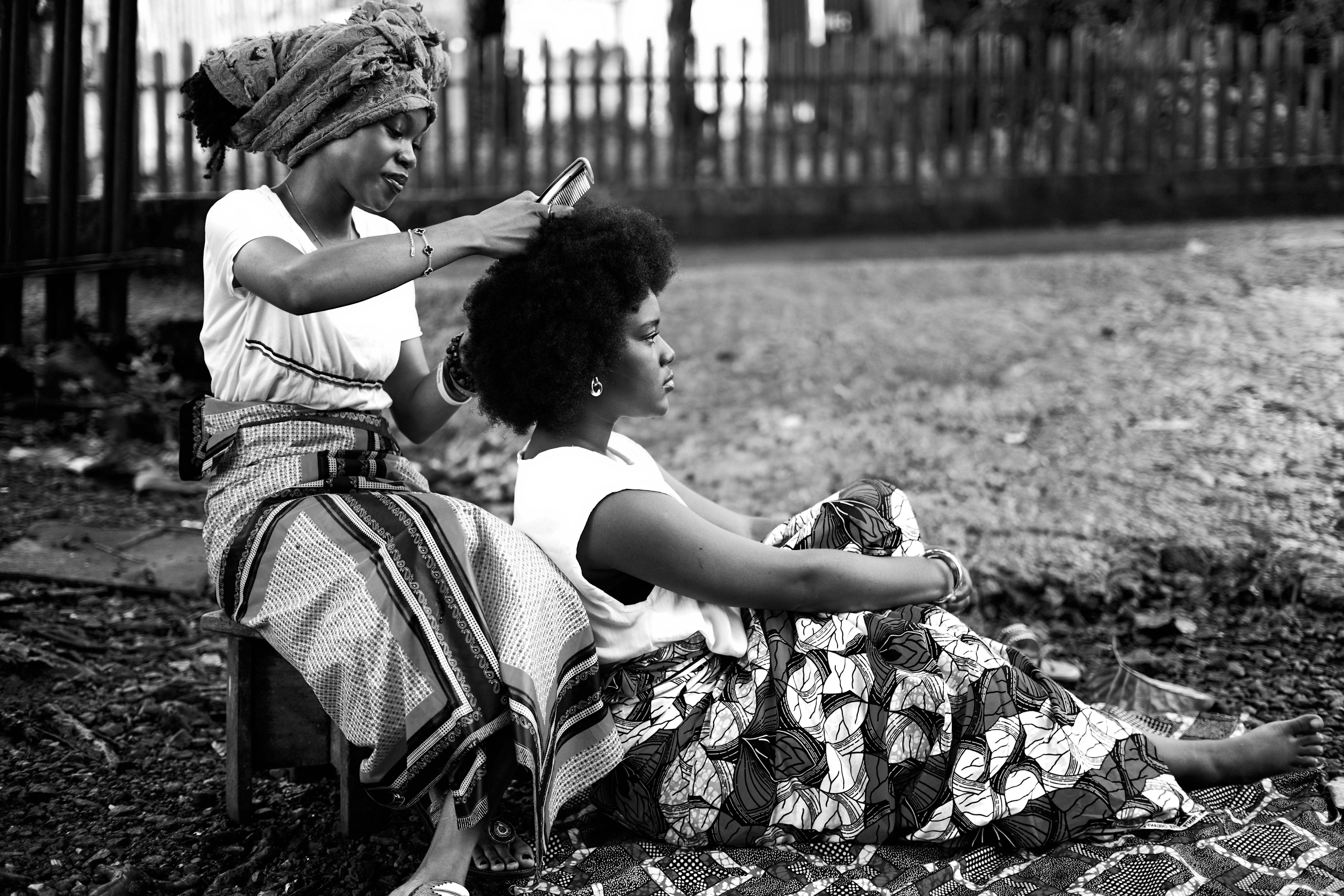Afro hair specialist braiding a client's hair outdoors in black and white